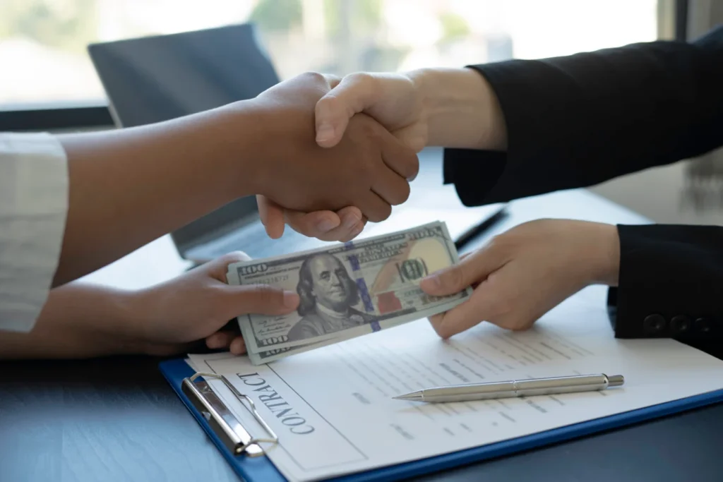 Handshake between two people as cash is exchanged over a signed contract, representing emergency cash loans in Singapore with quick approval.