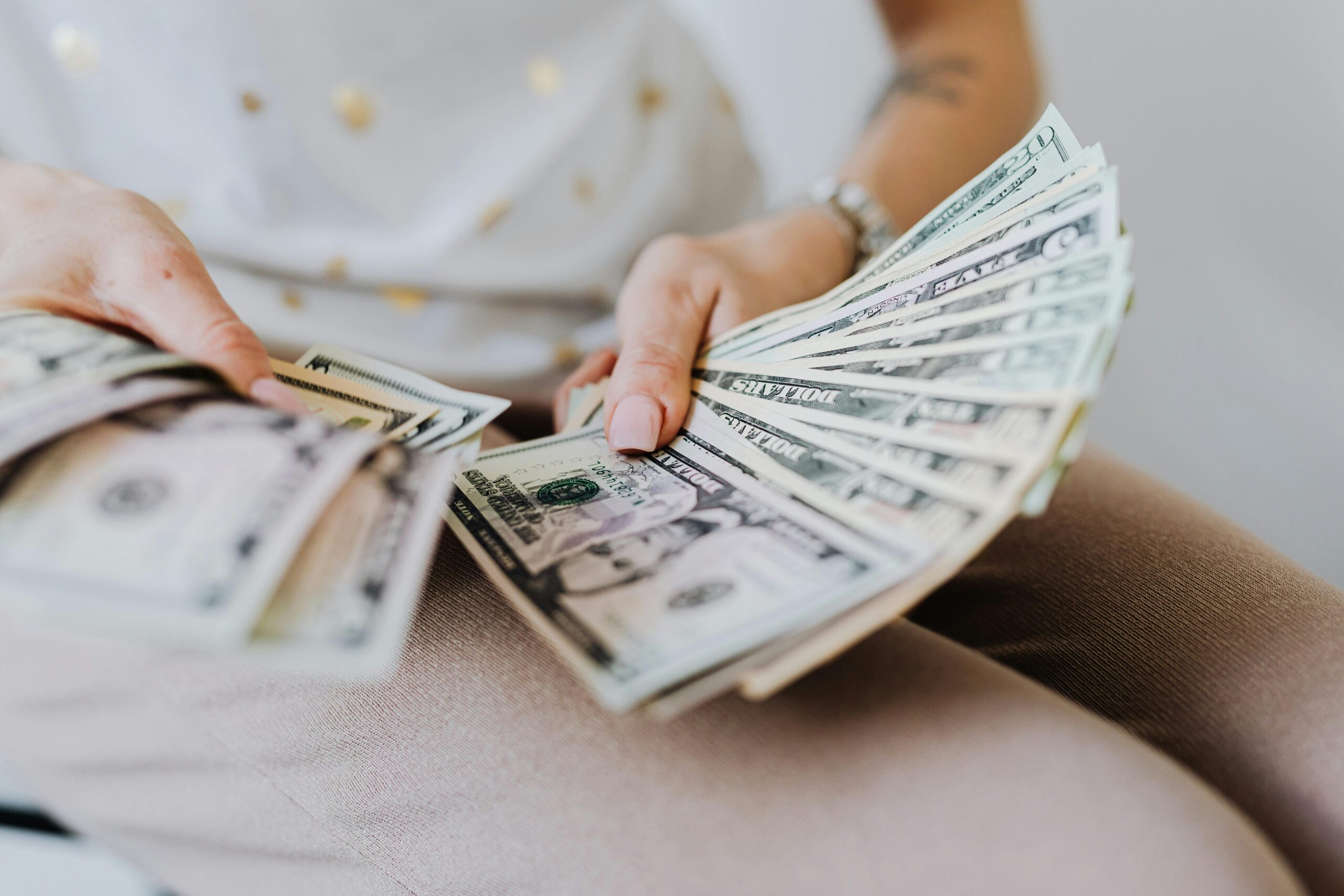 Person holding and counting multiple US dollar bills, representing financial concepts related to foreigners getting loans in Singapore.