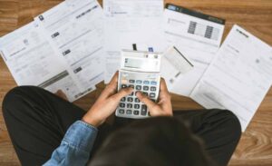 Person calculating bills with a calculator and documents spread on the floor.