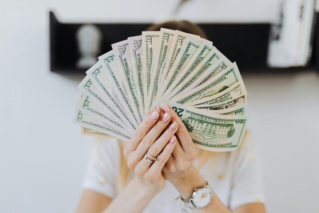 Person holding a fan of U.S. dollar bills in front of their face, symbolizing financial stress or money concerns related to missed loan payments.