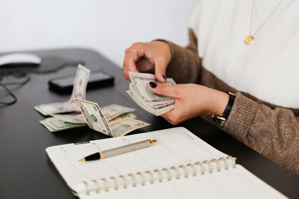 Person counting cash beside a planner notebook, representing the 50/30/20 budget method for managing loan instalments and monthly bills.