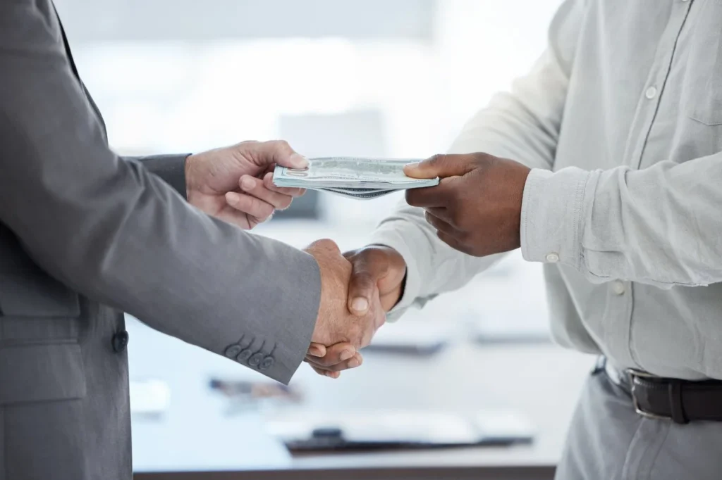 Person handing cash while shaking hands, symbolizing managing financial emergencies and money support.