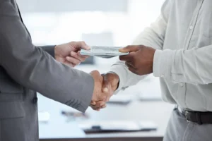 Person handing cash while shaking hands, symbolizing managing financial emergencies and money support.
