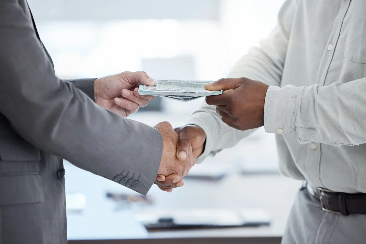Person handing cash while shaking hands, symbolizing managing financial emergencies and money support.