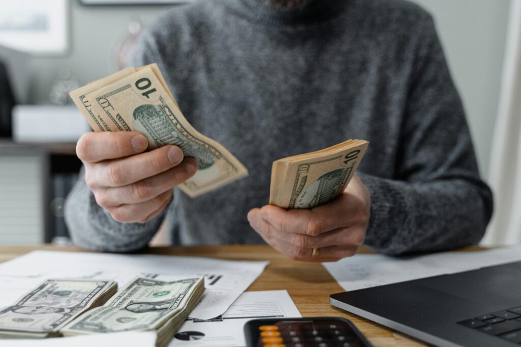 Person counting US dollar cash at a desk with documents, laptop, and calculator, representing financial stress and need for quick legal cash solutions.