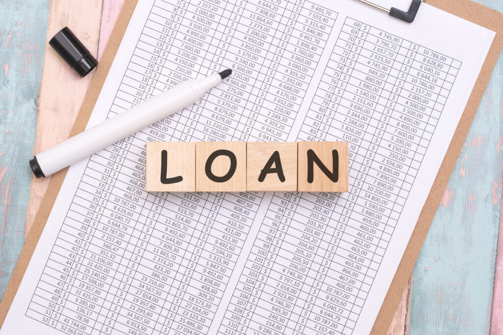 Loan concept with wooden blocks spelling ‘loan’ on financial documents, illustrating choosing the right loan type based on real-life expenses.