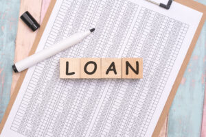 Loan concept with wooden blocks spelling ‘loan’ on financial documents, illustrating choosing the right loan type based on real-life expenses.