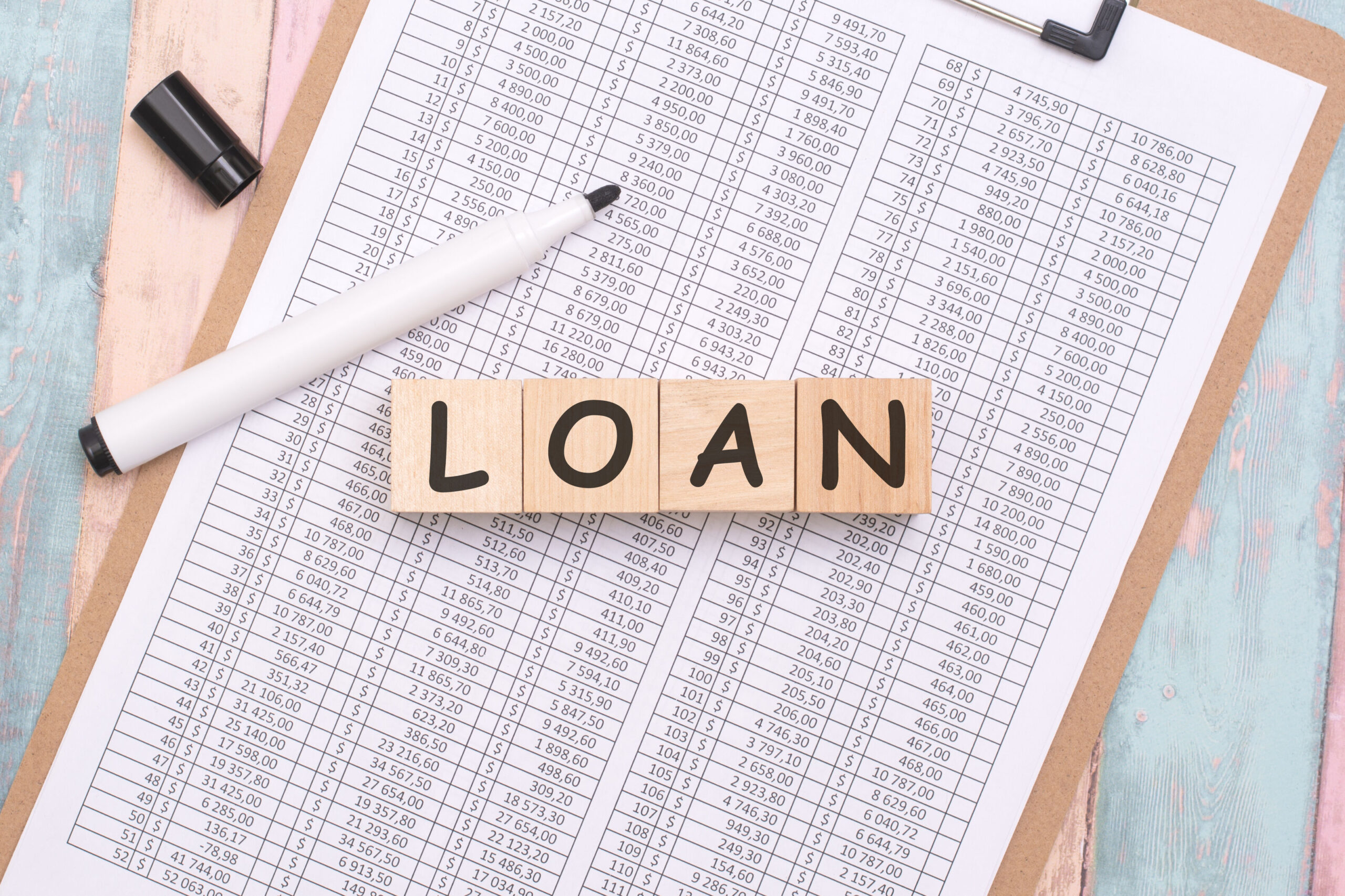 Loan concept with wooden blocks spelling ‘loan’ on financial documents, illustrating choosing the right loan type based on real-life expenses.
