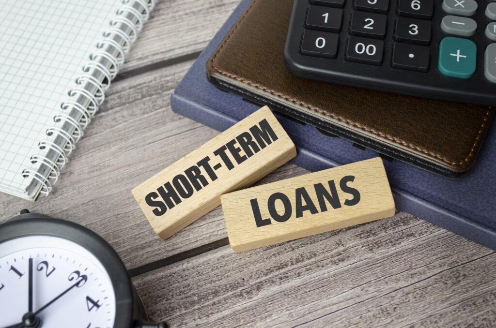 Short-term loan concept with wooden blocks labelled SHORT-TERM and LOANS beside a calculator, notebook, wallet, and clock, illustrating quick borrowing and short-duration financing in Singapore.