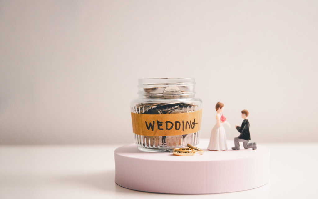 Wedding savings jar with coins, bride and groom figures, and wedding rings for funding a big day