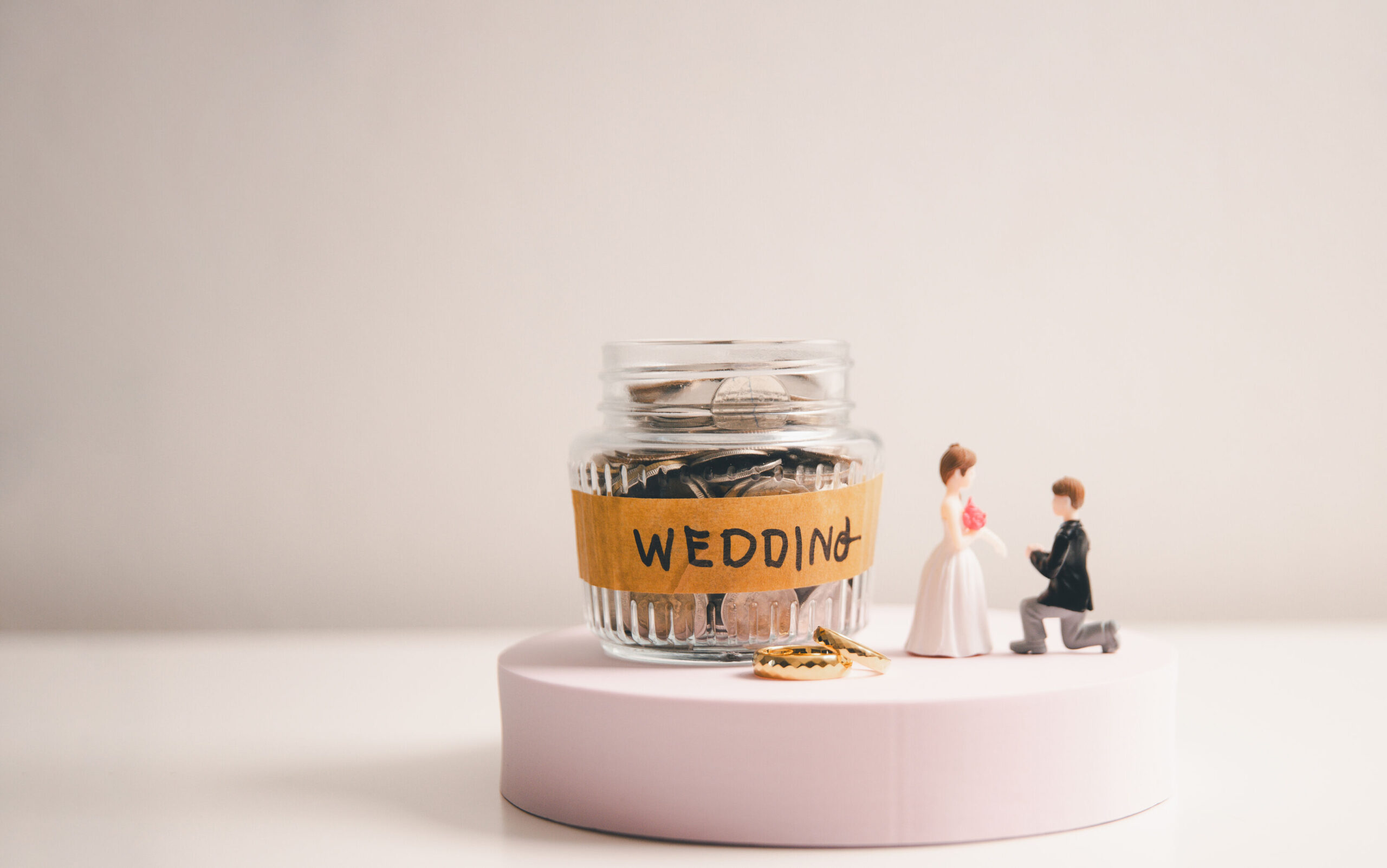 Wedding savings jar with coins, bride and groom figures, and wedding rings for funding a big day