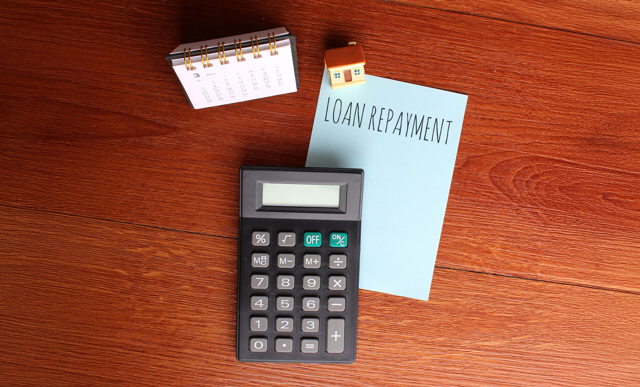 Loan repayment planning with a calculator, calendar and repayment note, illustrating the cost of extending a loan over a longer repayment period.